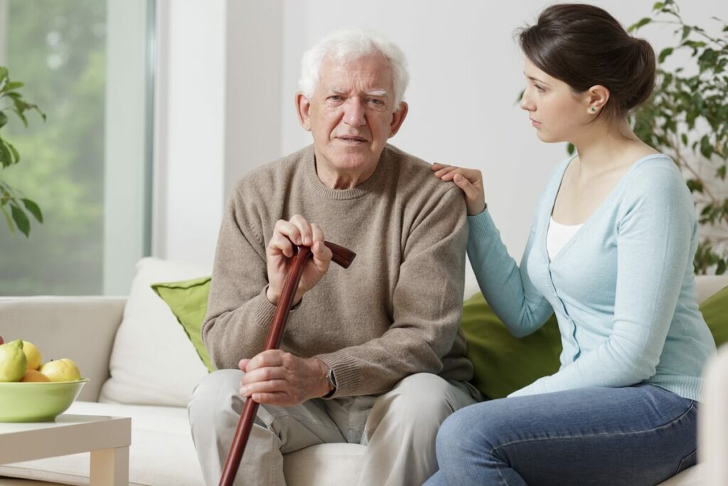 SoCo Village | Senior man with a cane sitting down next to his caregiver